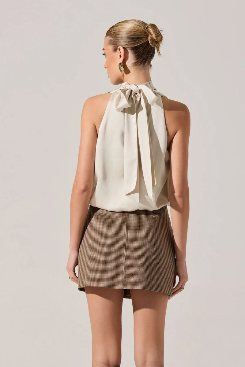 Woman wearing a beige halter top and brown skirt against a plain background.
