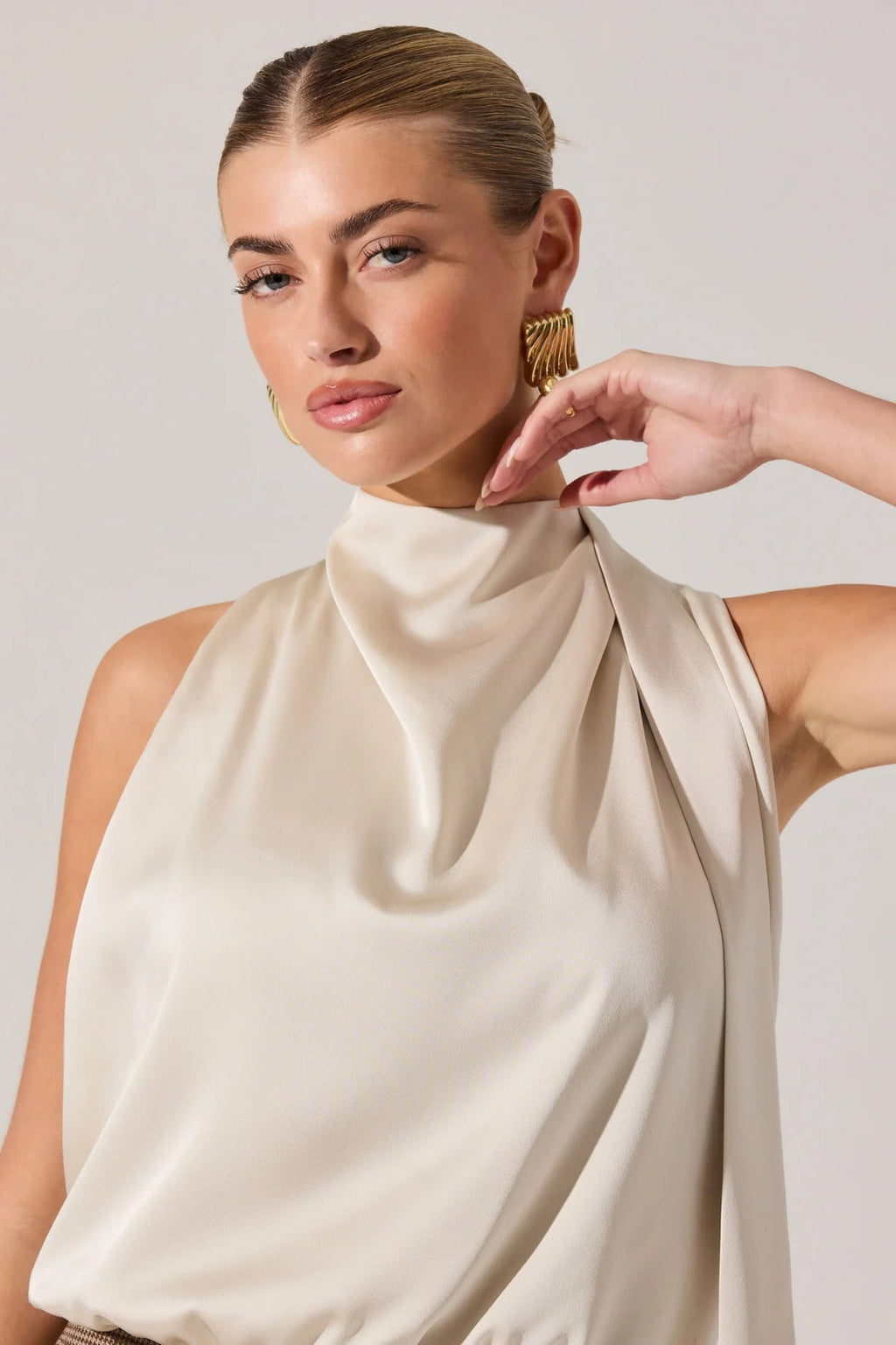 Woman wearing a beige sleeveless top with a plain background.
