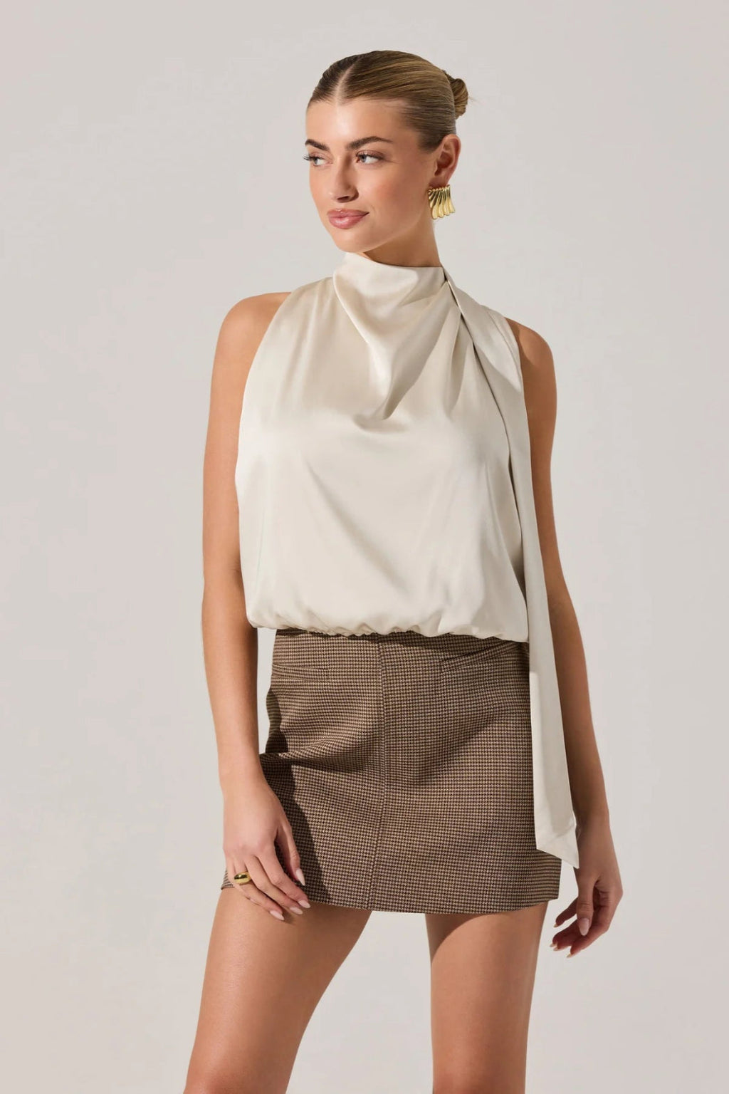 Woman wearing a white sleeveless top and brown checkered skirt on a plain background.
