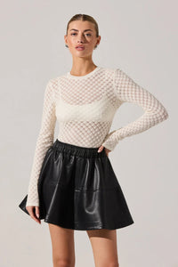 Woman wearing a white textured sweater and black leather skirt on a plain background.