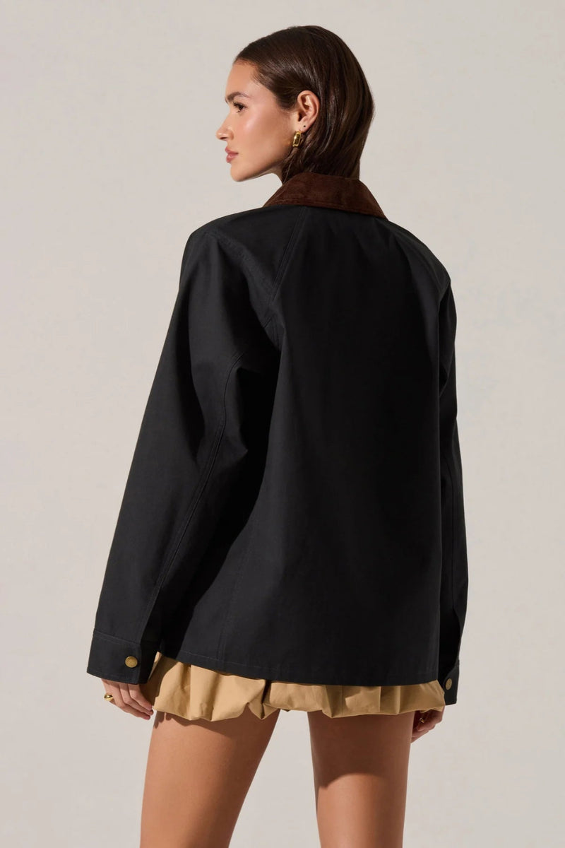 Woman wearing a black jacket and gold shorts on a plain background.