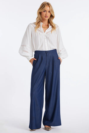 Woman wearing a white blouse and blue pants on a white background.