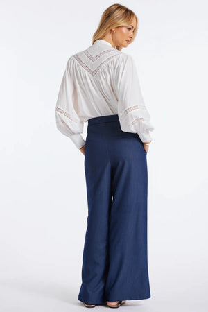 Woman wearing a white blouse with lace details and navy blue pants on a white background.