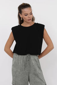 Woman wearing a black sleeveless top and gray pants on a white background.