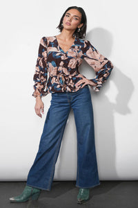 Woman wearing a patterned blouse and blue jeans against a white background.