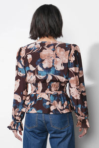 Person wearing a floral blouse with long sleeves and blue jeans on a white background.