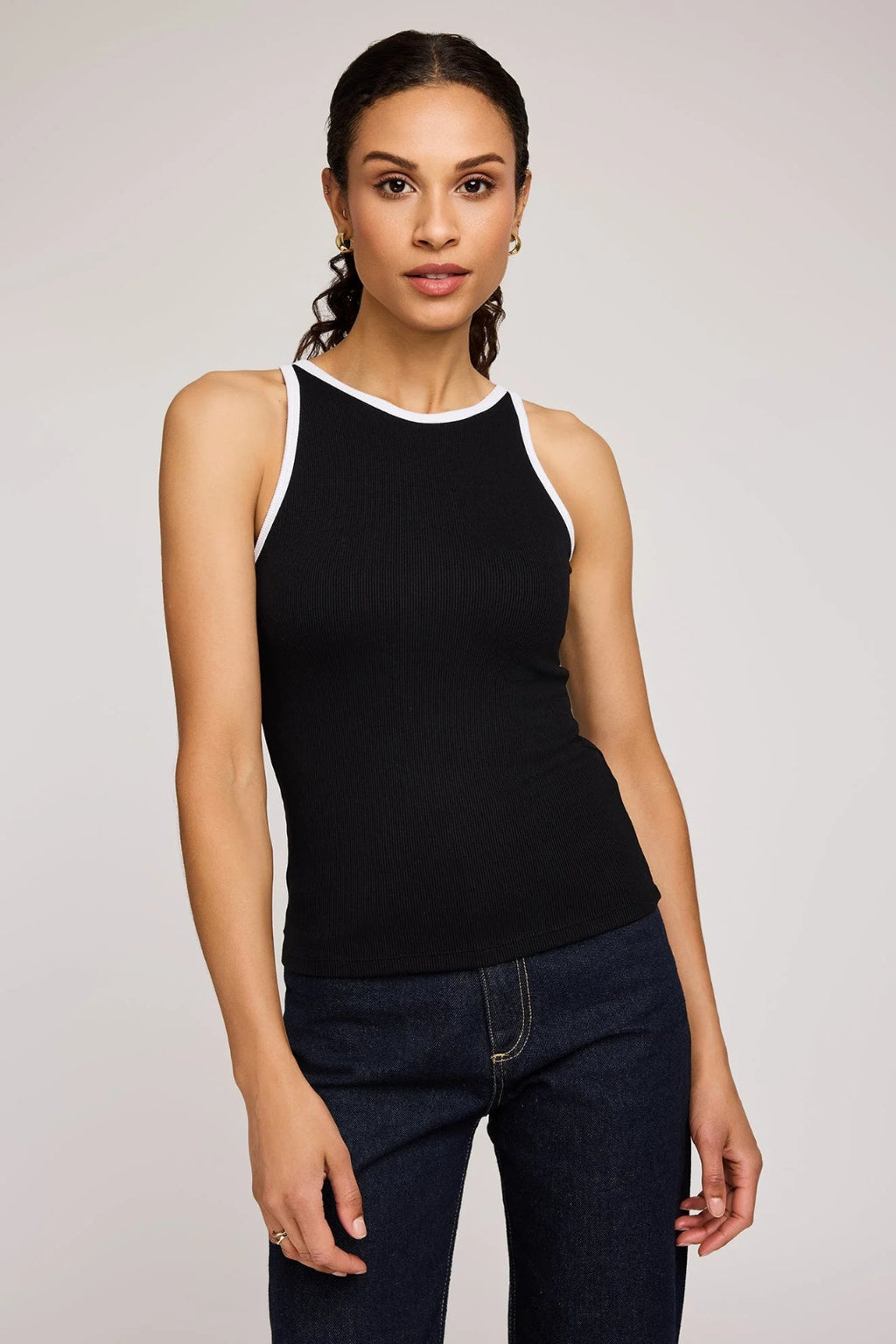 Woman wearing a black tank top and blue jeans against a plain background