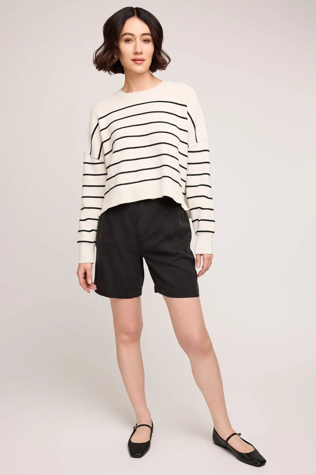 Woman wearing a black and white striped sweater with black shorts on a plain background.