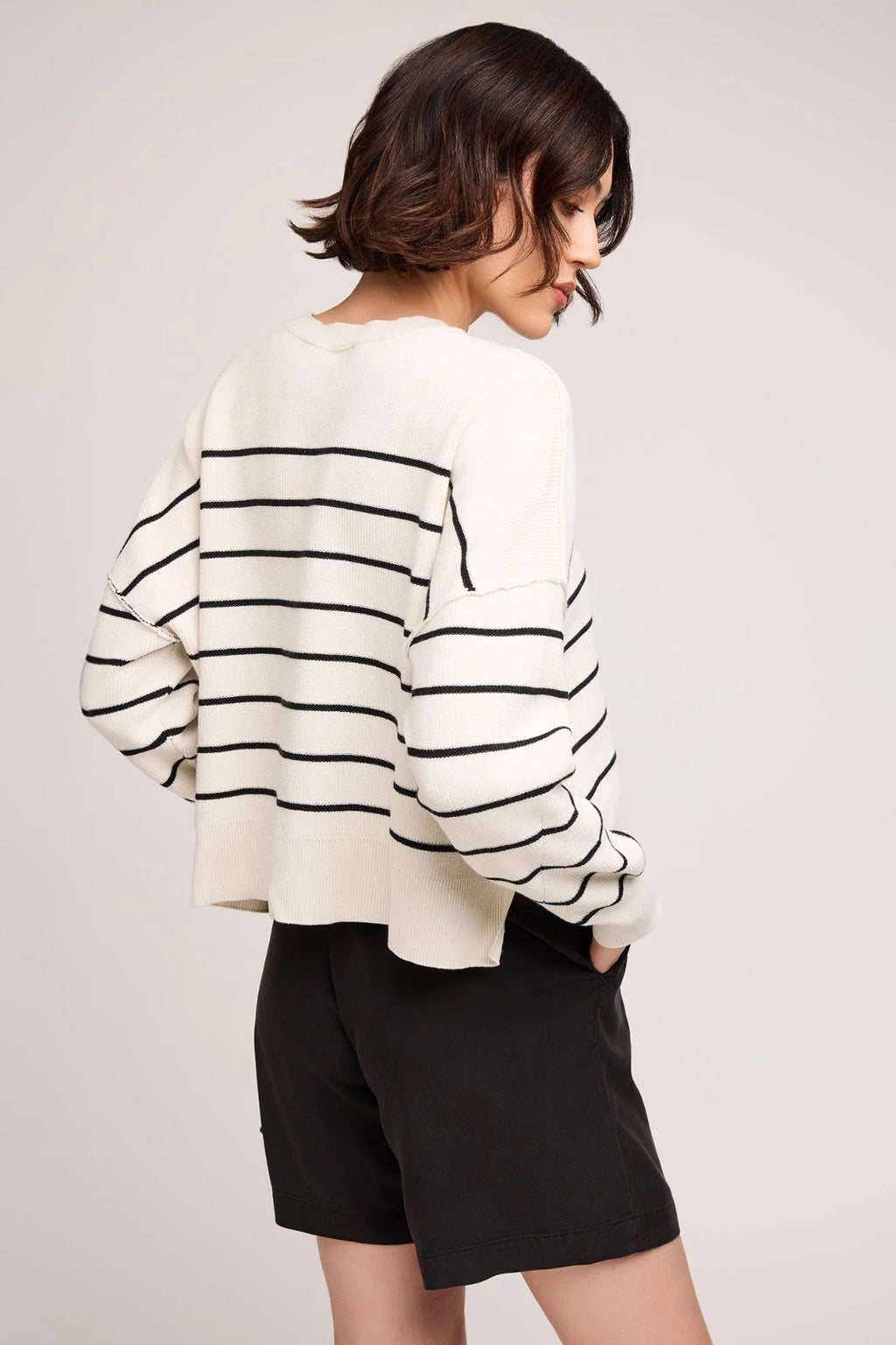 Person wearing a white sweater with black stripes and black shorts on a light gray background.