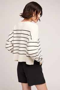 Person wearing a white sweater with black stripes and black shorts on a light gray background.