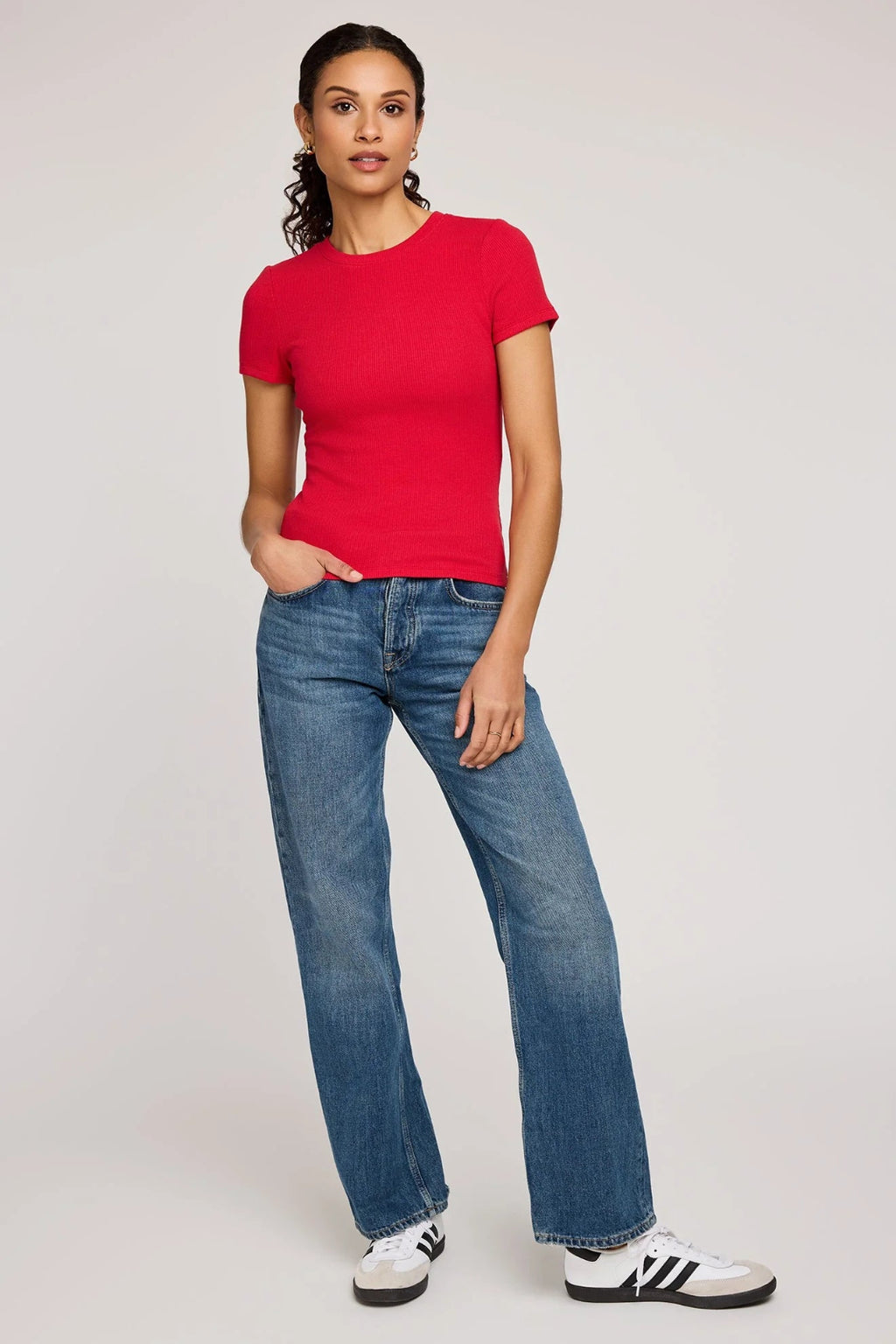 Woman wearing a red t-shirt and blue jeans on a plain background.