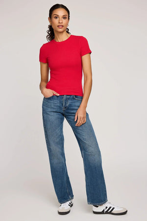 Woman wearing a red t-shirt and blue jeans on a plain background.