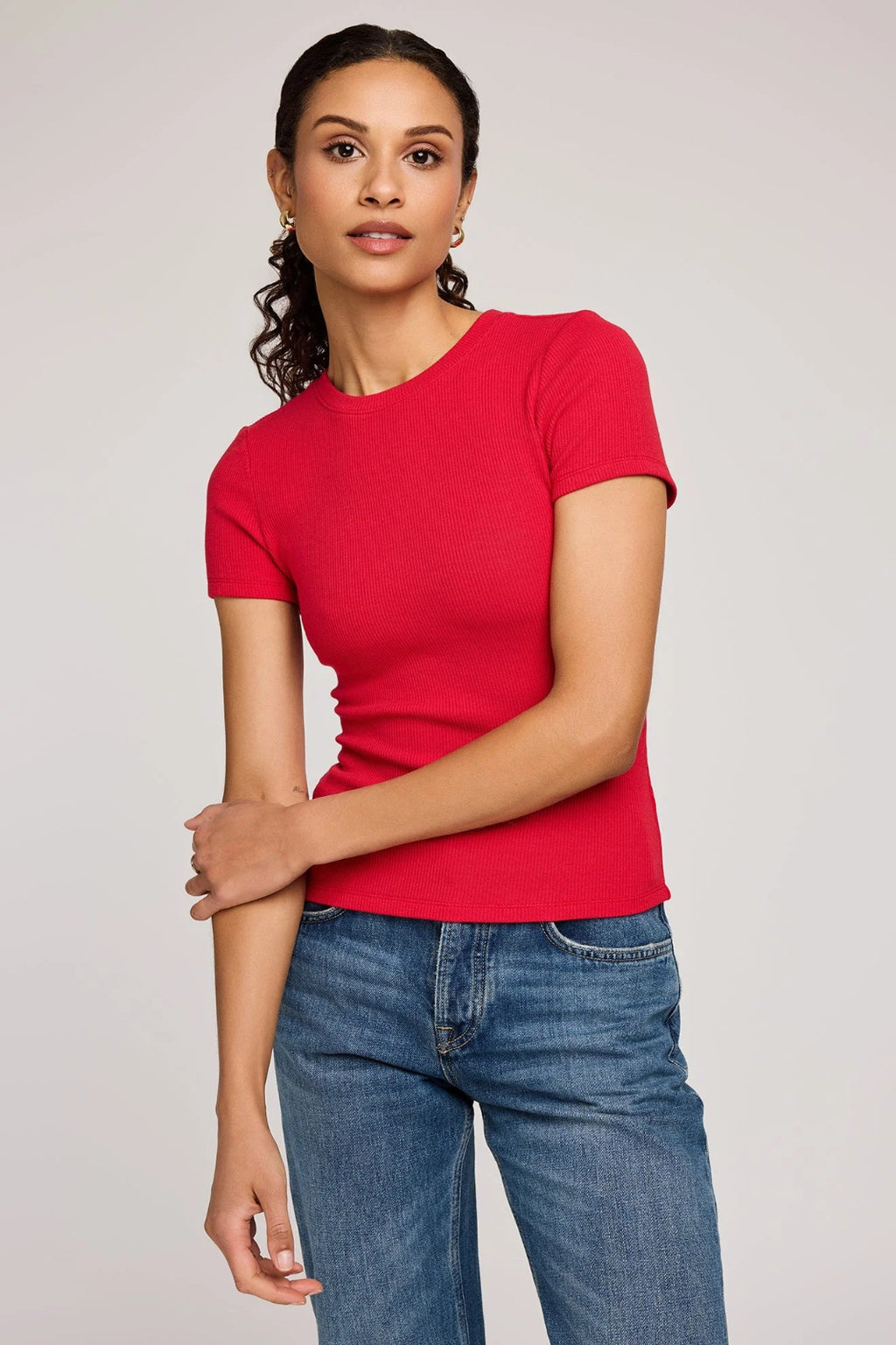 Woman wearing a red t-shirt and blue jeans on a plain background.