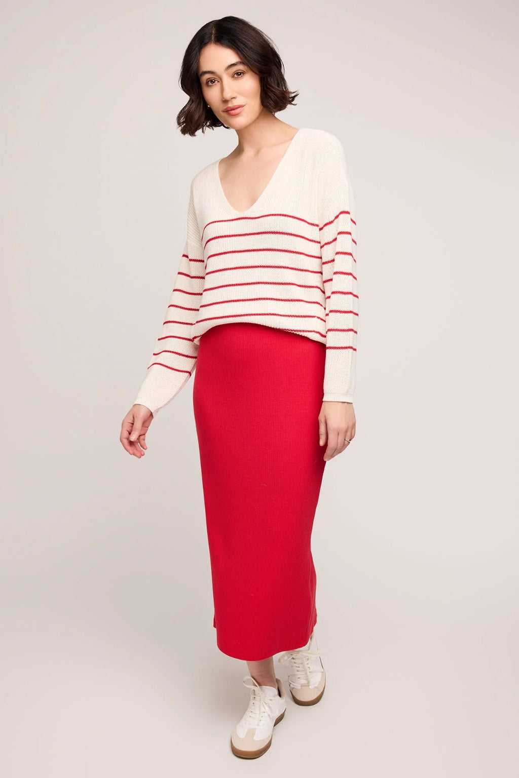 Woman wearing a red and white striped sweater with a red skirt on a light gray background.