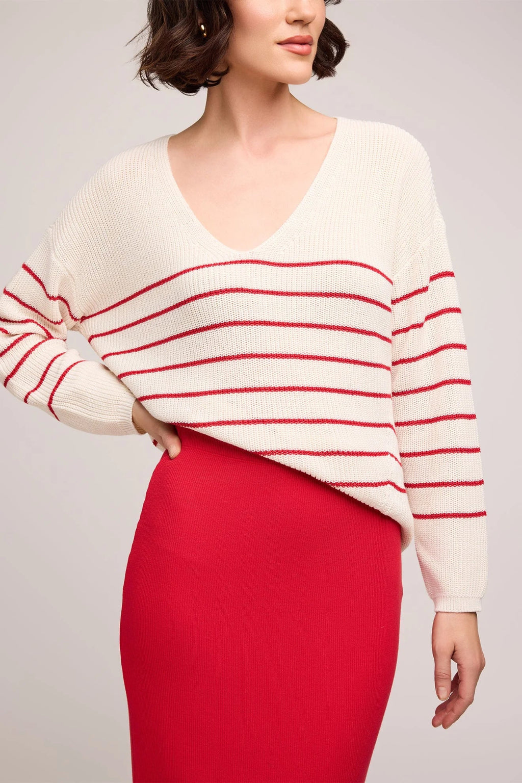 Woman wearing a white sweater with red stripes and a red skirt on a light gray background.