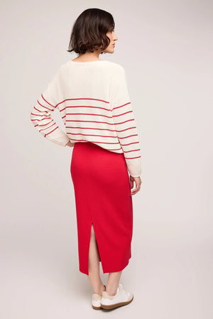 Woman wearing a white sweater with red stripes and a red skirt on a light gray background.