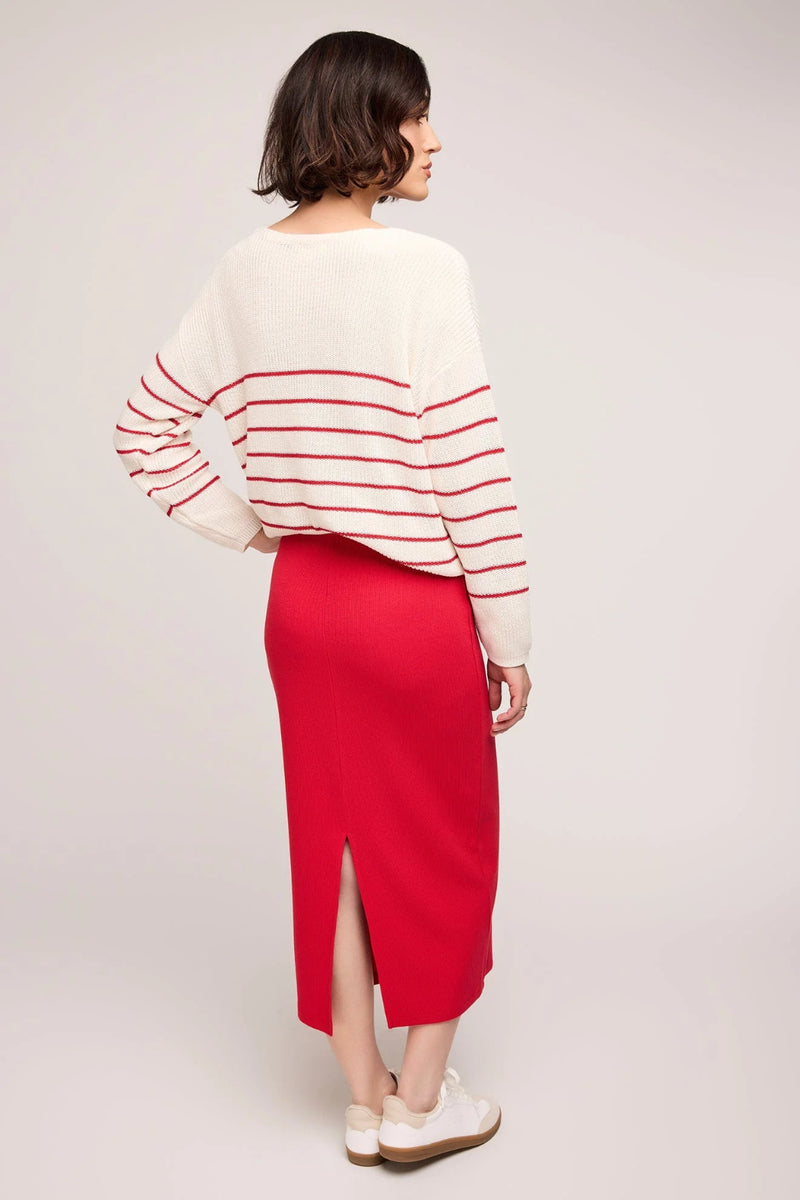 Woman wearing a white sweater with red stripes and a red skirt on a light gray background.