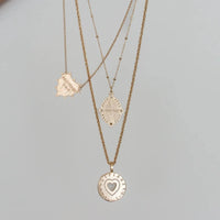 Three gold necklaces with heart pendants on a light gray background