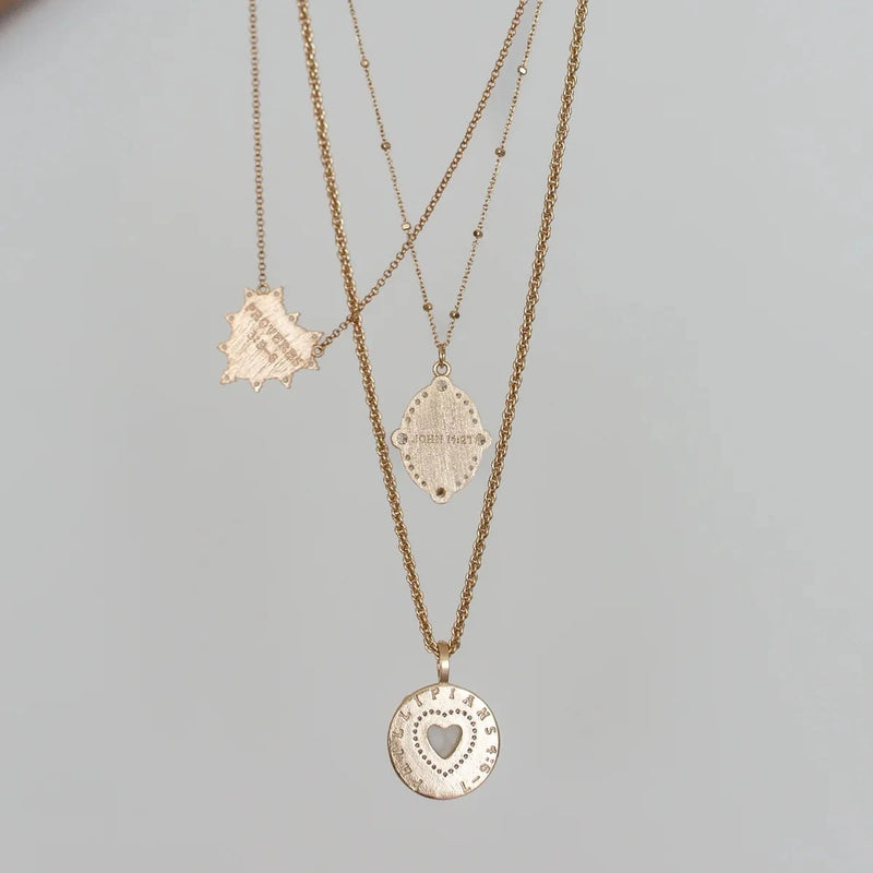 Three gold necklaces with heart pendants on a light gray background