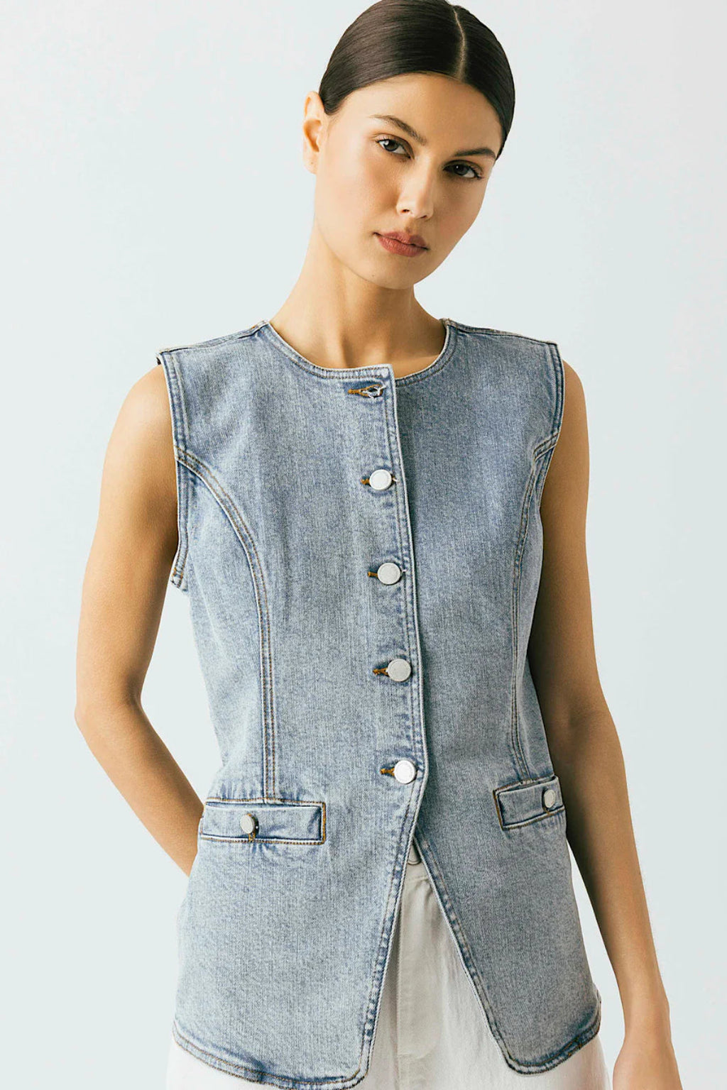 A woman wearing a denim vest with white pants.