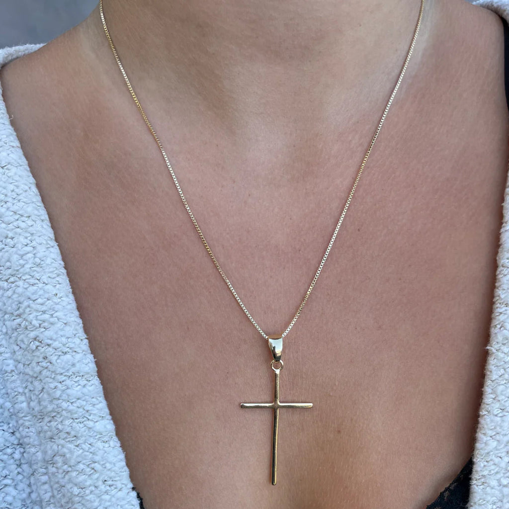 Gold cross necklace on a person's neck against a neutral background