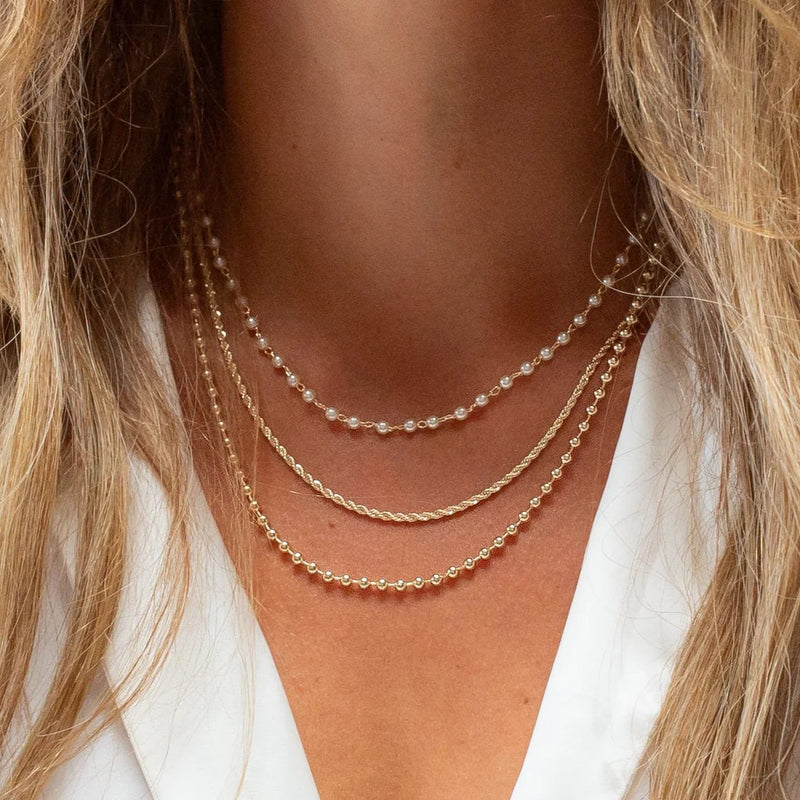 Close-up of a person wearing multiple gold necklaces with a blurred background.