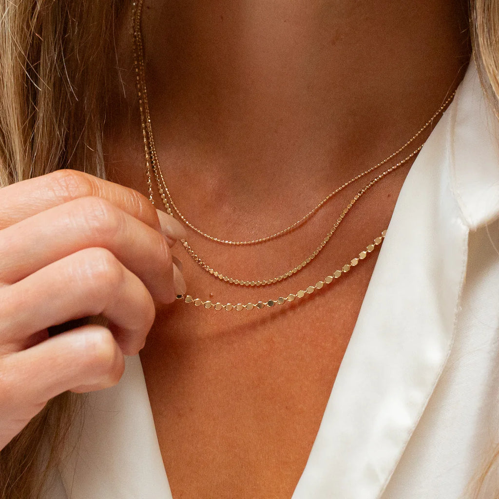 Close-up of a person wearing a gold necklace with a white shirt.