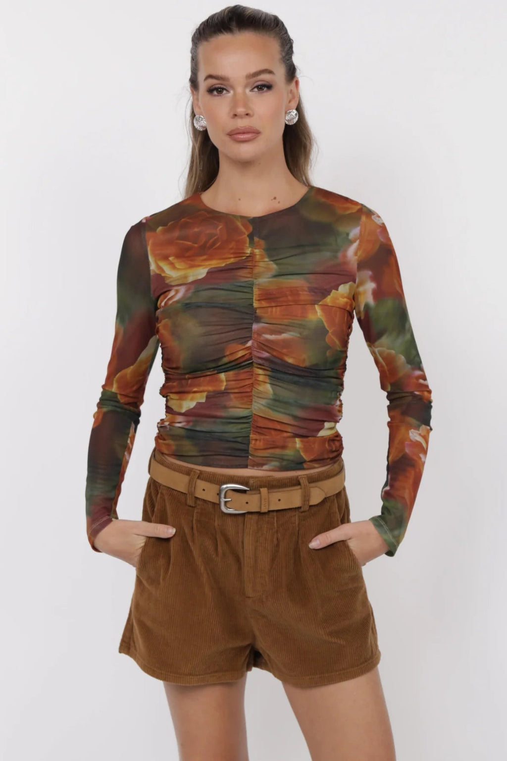 Woman wearing a patterned long-sleeve top and brown shorts on a white background.