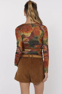 Person wearing a colorful floral long-sleeve top and brown shorts on a white background.