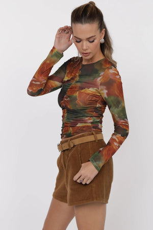 Woman wearing a long-sleeve floral top and brown shorts on a white background.