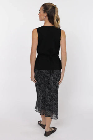 Woman wearing a black sleeveless top and patterned skirt on a white background.