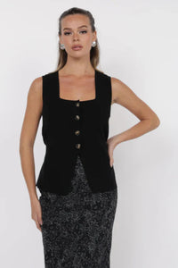 Woman wearing a black sleeveless top with buttons on a white background.