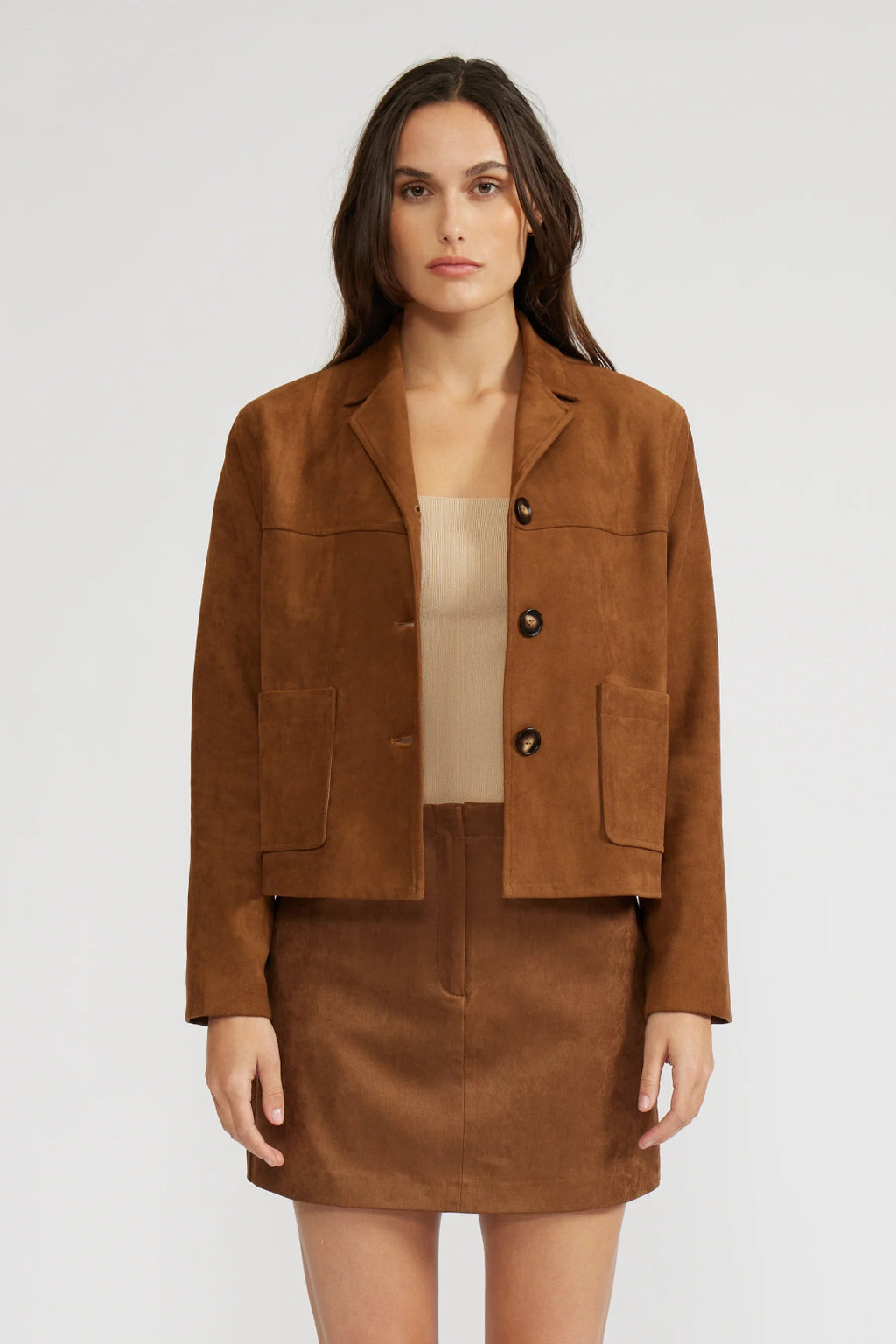 Woman wearing a brown suede jacket and skirt set on a white background.