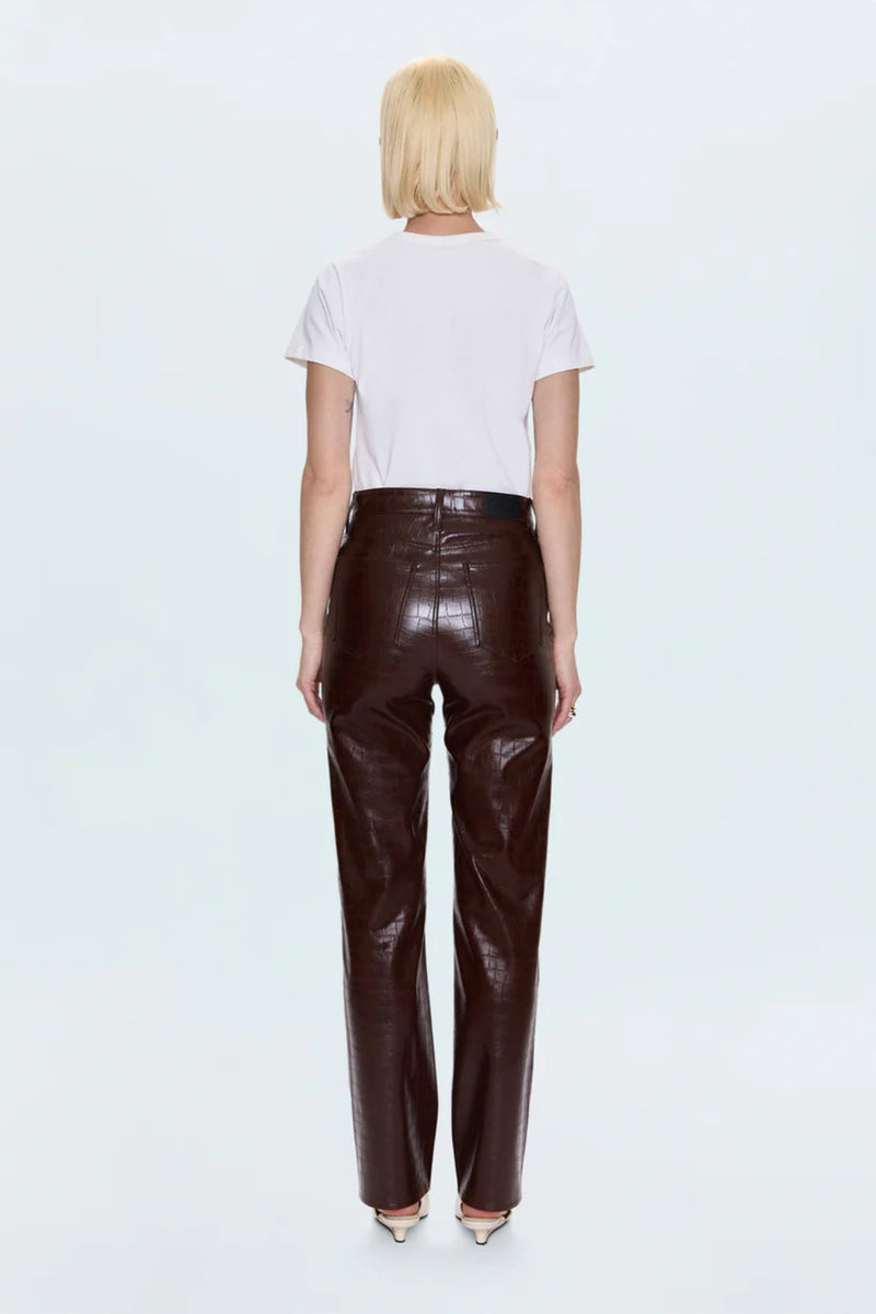 Person wearing a white t-shirt and brown leather pants on a light gray background.