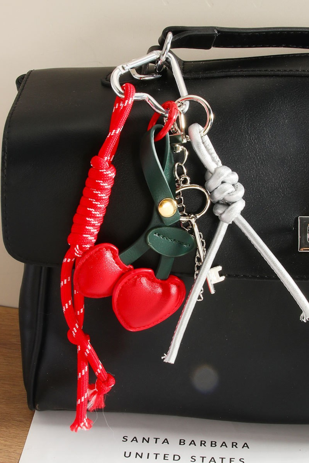 Red cherry bag charm hanging on a black purse.