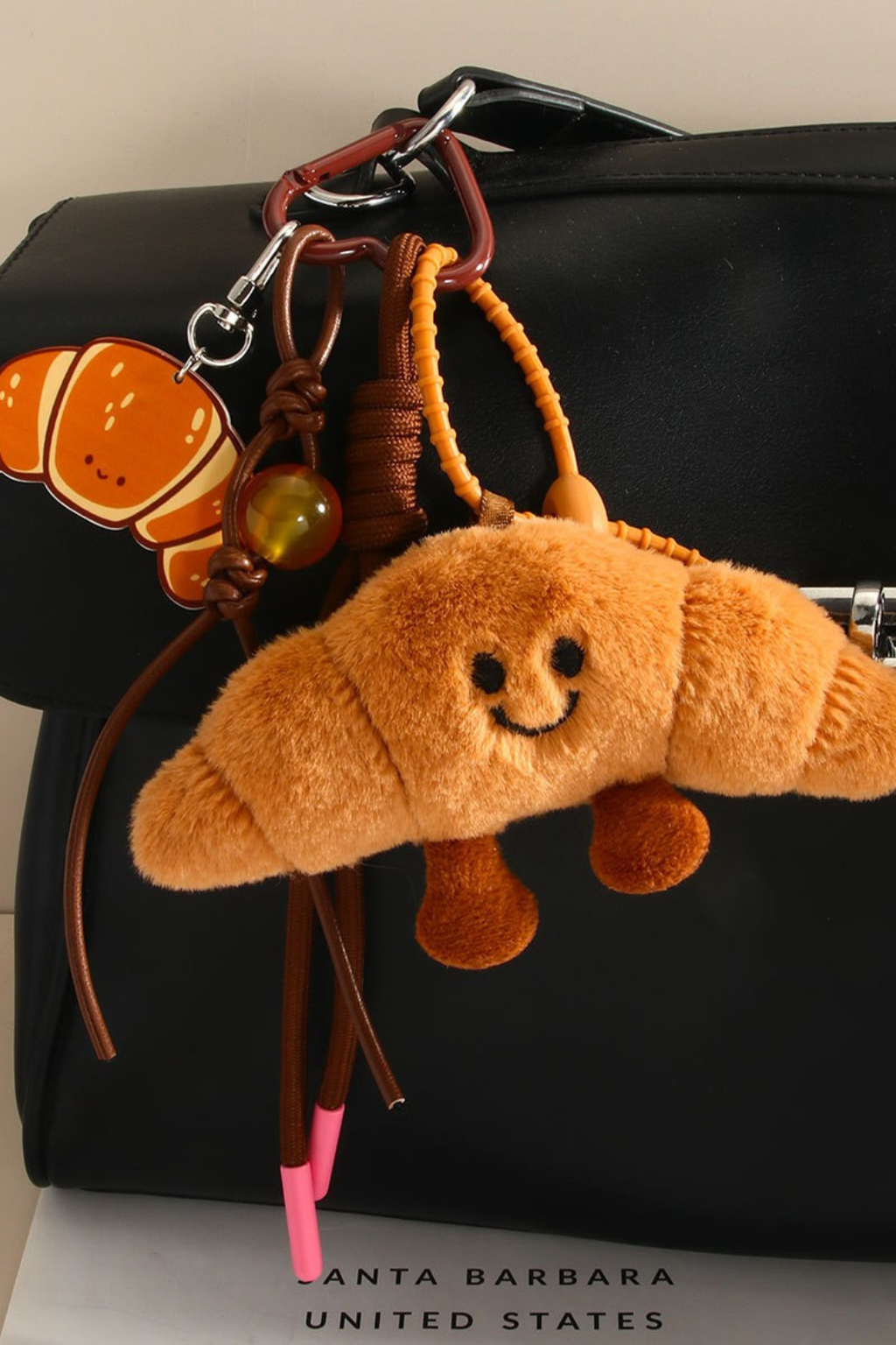 Plush croissant keychain attached to a black bag.