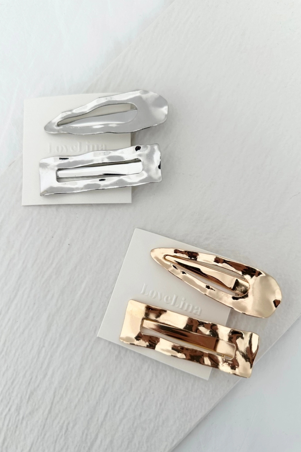Two silver hair clips and two gold hair clips on a light gray background.