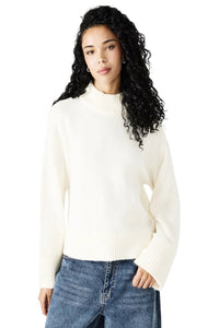 Woman wearing a white turtleneck sweater and blue jeans on a white background.