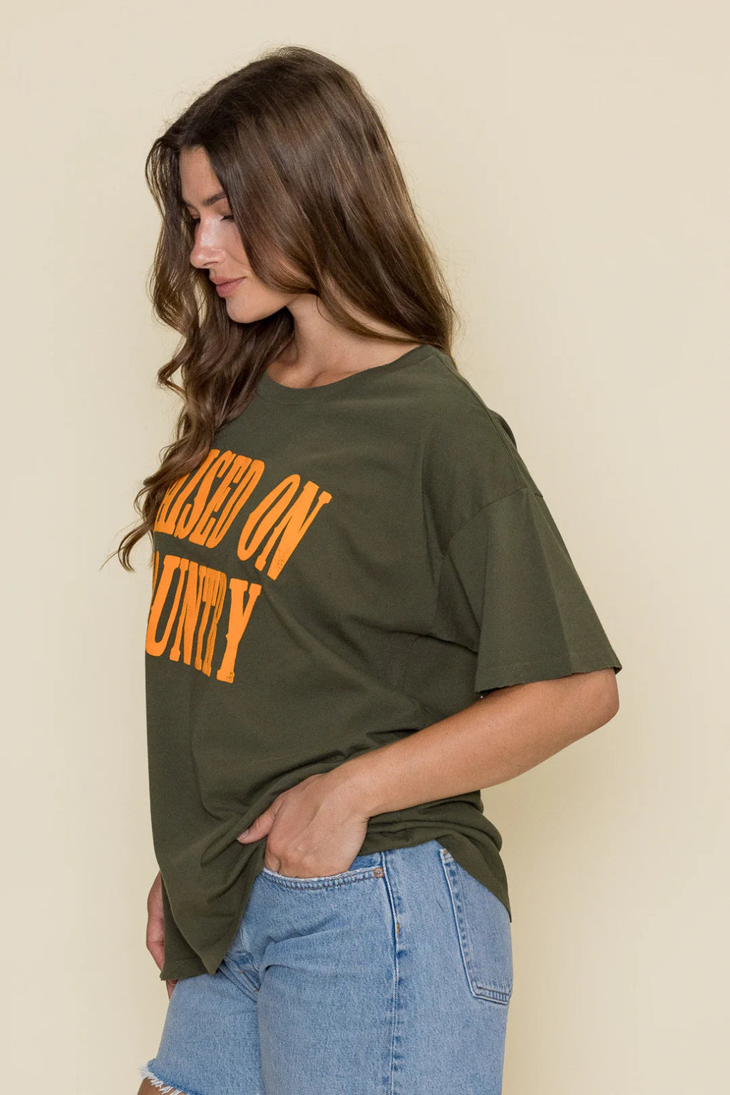 Side view of a woman wearing a green shirt with orange writing and denim shorts.
