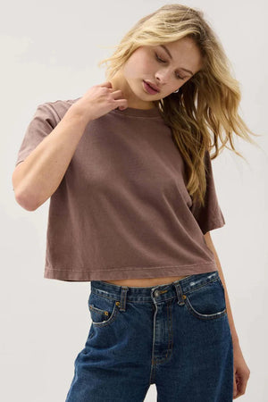 Woman wearing a brown cropped t-shirt and blue jeans against a white background.
