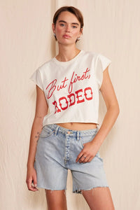 A woman wearing a white shirt with red lettering, and denim shorts.