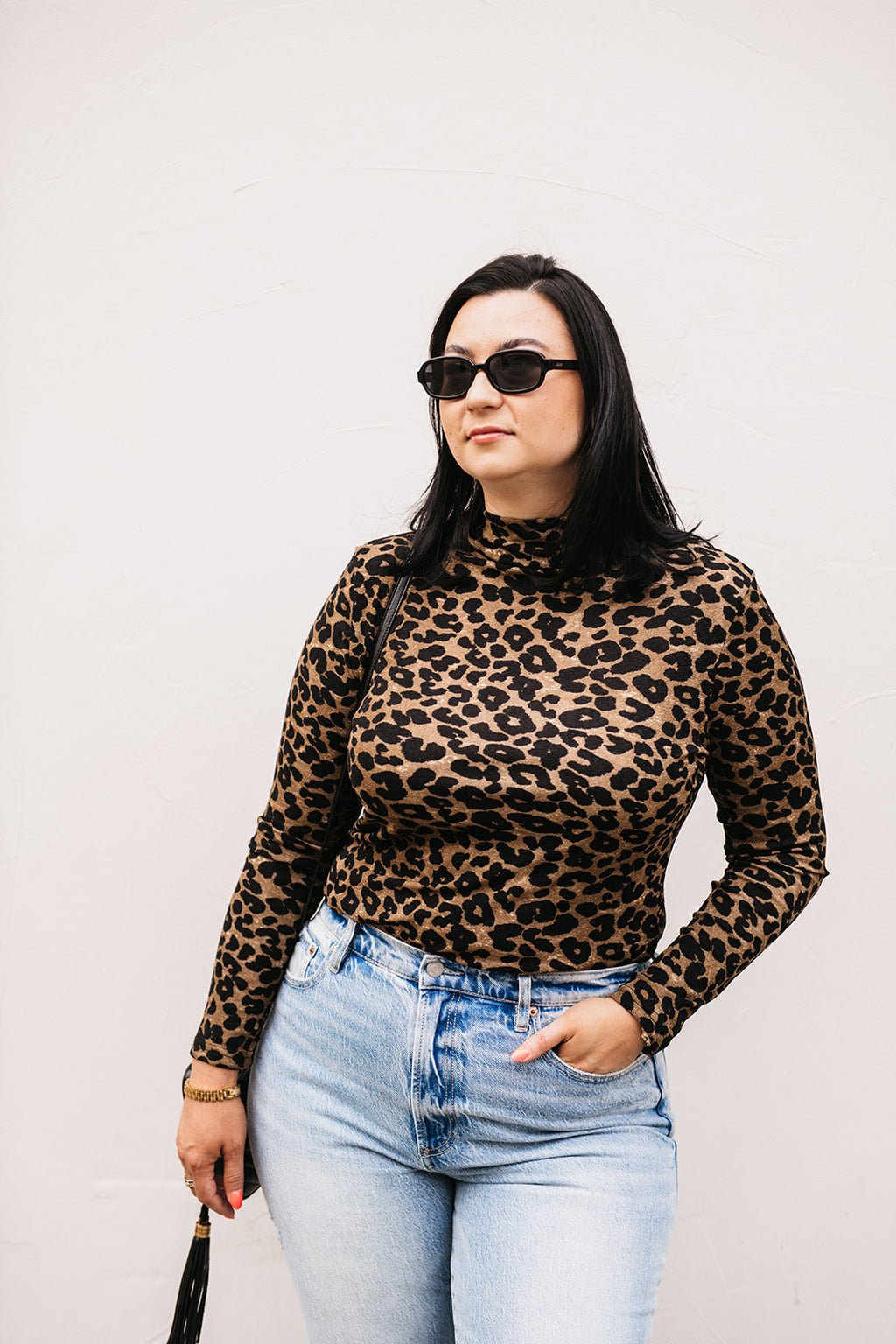 Person wearing a leopard print top and light blue jeans against a plain background