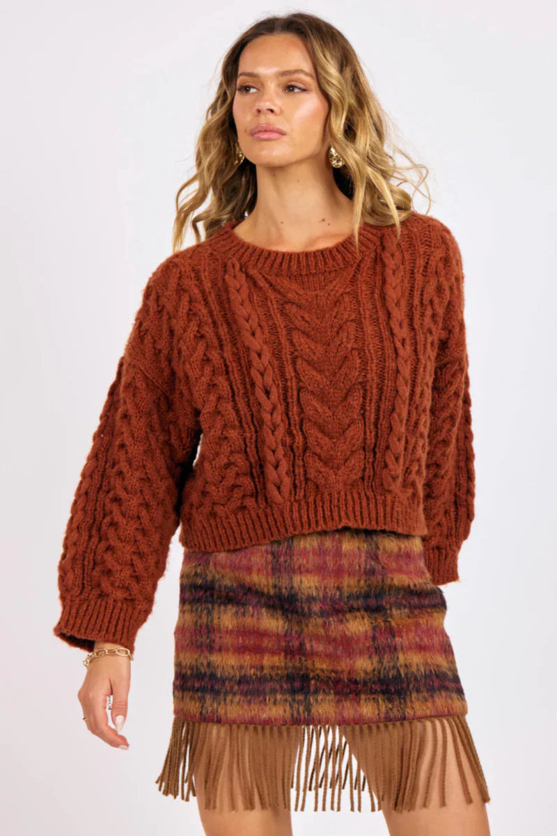 Woman wearing a brown knitted sweater and plaid skirt on a white background.