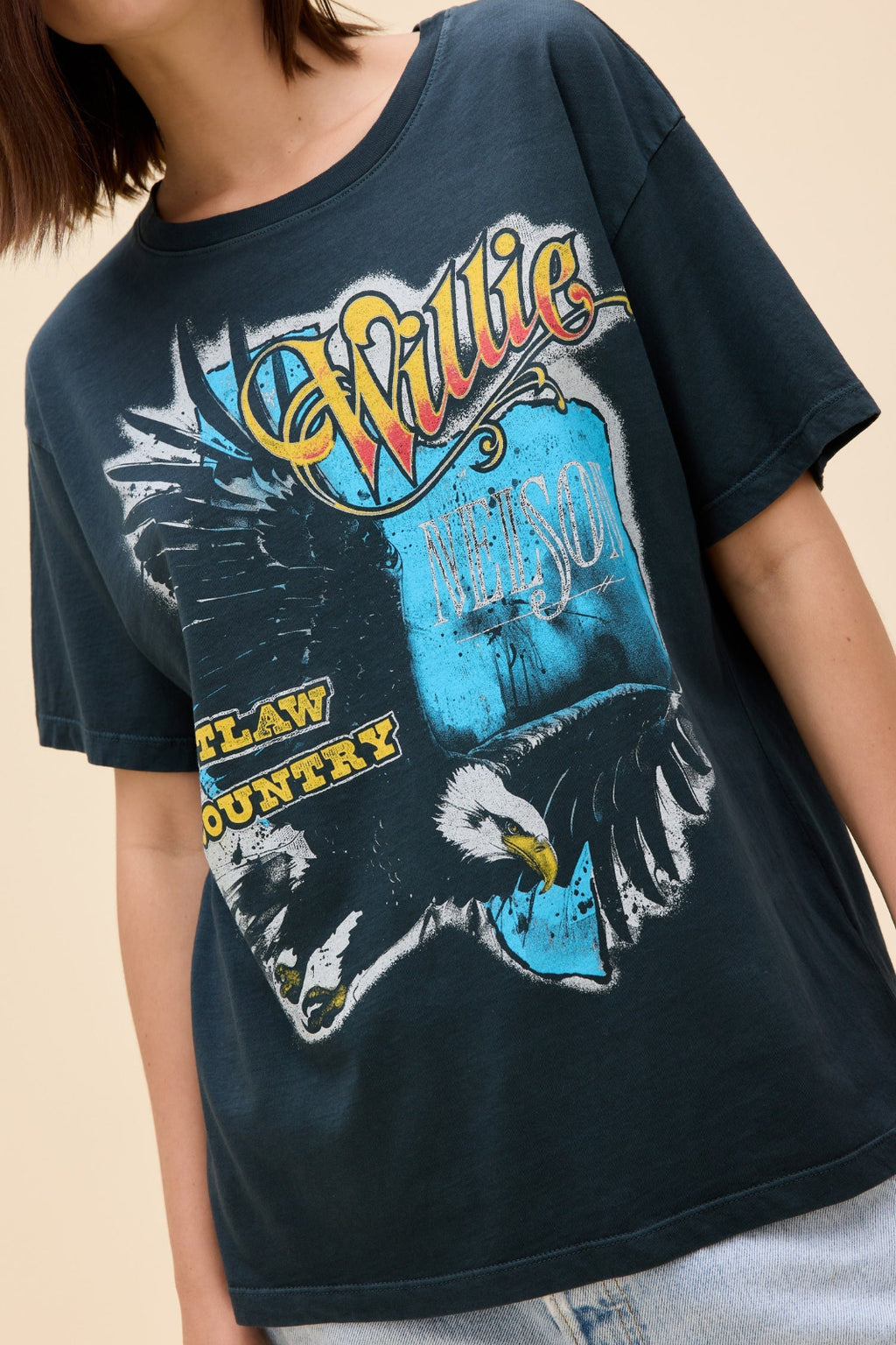 Close up view of a woman wearing a navy blue Willie Nelson graphic tee and denim shorts.