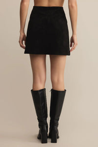 Person wearing a black mini skirt and knee-high black boots on a beige background.