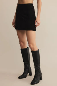 Person wearing a black mini skirt and knee-high black boots on a beige background