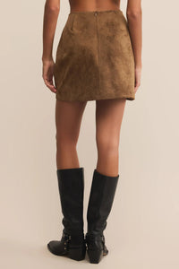 Person wearing a brown suede skirt and black knee-high boots on a beige background.