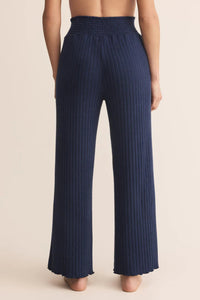 Navy pleated pants worn by a person on a beige background.