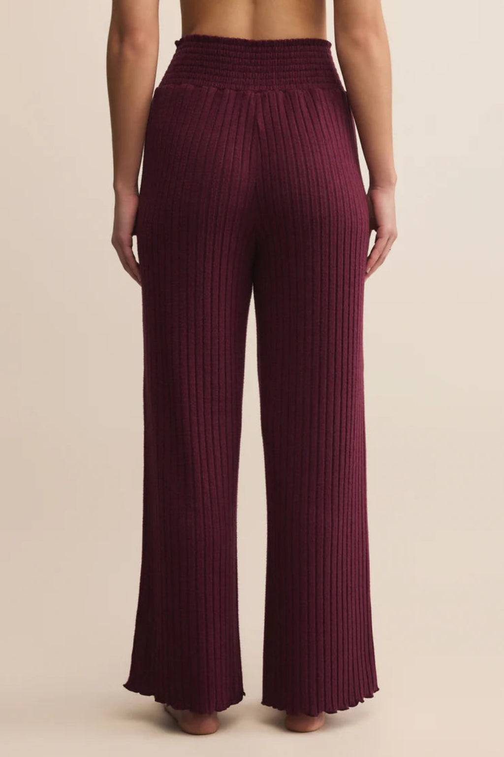 Maroon ribbed pants worn by a person on a beige background.