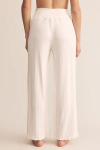 White pleated pants worn by a person on a beige background.